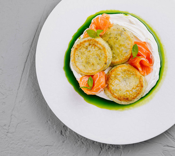 Bovenaanzicht van delicate viskoekjes geserveerd met een levendige kruidensaus en versierd met zalmstukjes - Foto, afbeelding