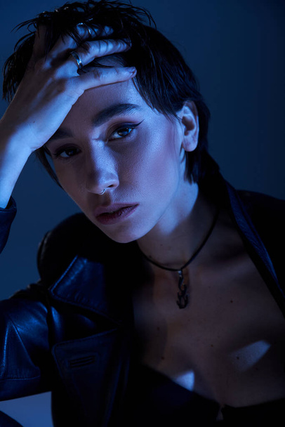 Stylish woman in black leather jacket with hands on head poses confidently. - 写真・画像