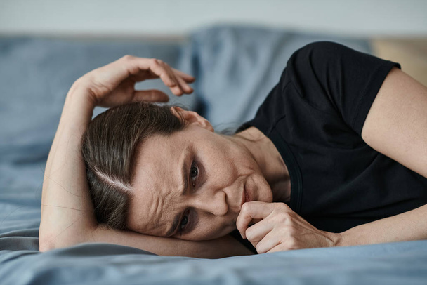 Middle-aged woman lays on bed, hand on head. - Valokuva, kuva