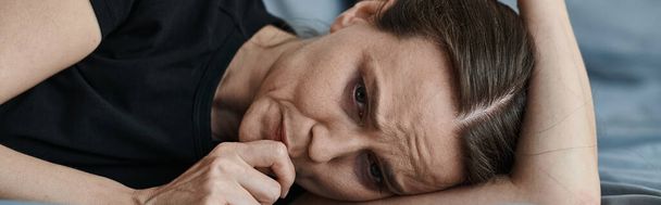 Middle-aged woman laying on bed with hand on head, deep in thought. - Foto, Bild