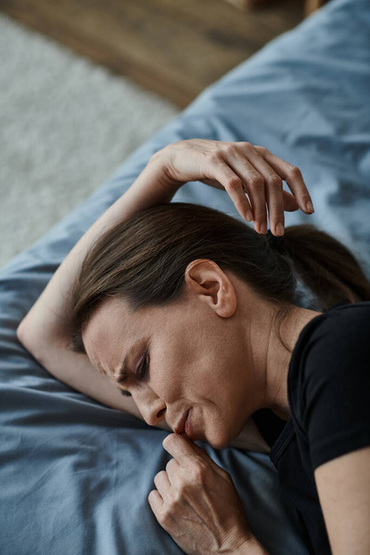 Middle-aged woman lying in bed, hand on head, lost in thought. - Foto, Bild