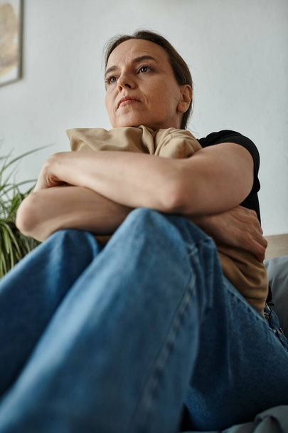 Middle-aged woman sits on couch with arms crossed. - Foto, Imagem