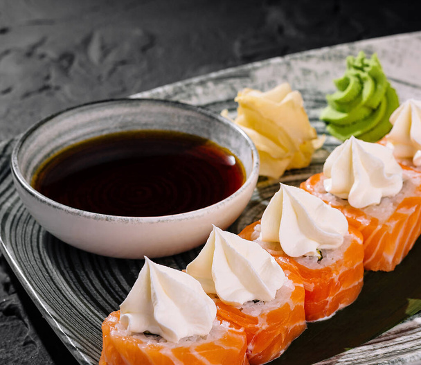 Элегантные суши с начинкой из сливочного сыра, подаются с соевым соусом, васаби и имбирем на шикарной тарелке - Фото, изображение