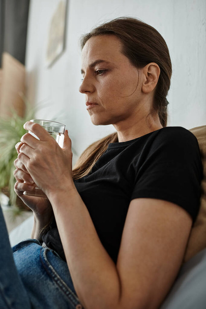 Woman in contemplation on couch holding water. - Foto, afbeelding