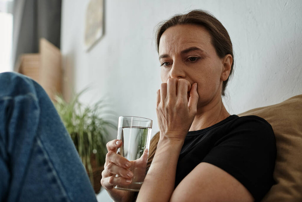 Woman finds solace, holding water on couch. - Fotoğraf, Görsel