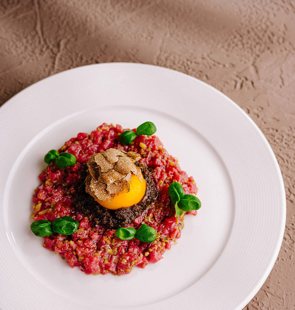 Elegant beef tartare topped with a quail egg and black truffle, served on a white plate - Photo, Image