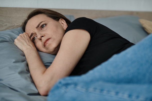 Middle-aged woman lying in bed, head propped on hand, lost in deep thought. - Foto, Bild