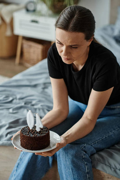 Woman holding a cake while sitting on her bed. - Фото, зображення
