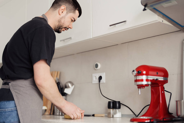 Skupiony mężczyzna w nowoczesnej kuchni przy użyciu czerwonego stoiska mikser do przygotowania makaronu. - Zdjęcie, obraz