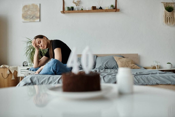 Middle-aged woman sitting with cake on bed, lost in thought. - Foto, immagini