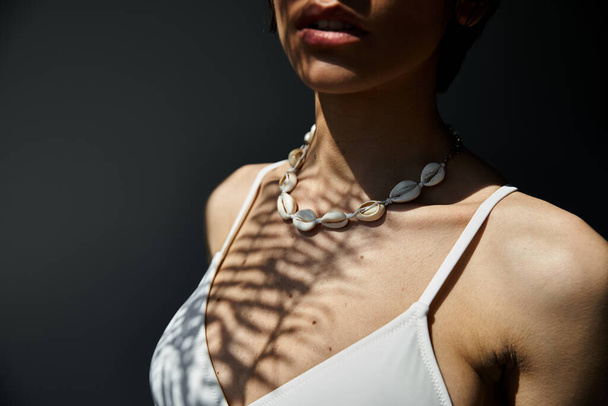 A woman adorned in a stylish seashell necklace poses gracefully. - Фото, зображення