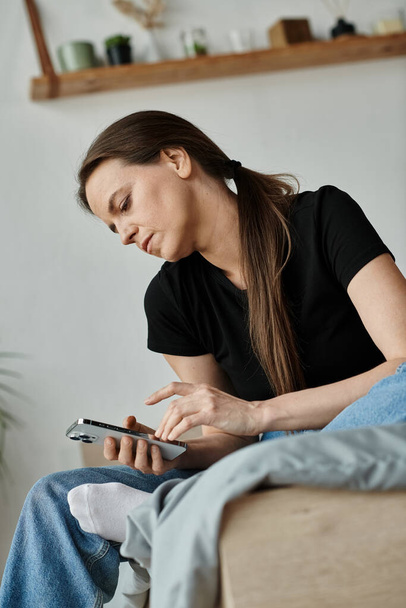 Middle-aged woman on couch, absorbed in phone screen. - Foto, afbeelding