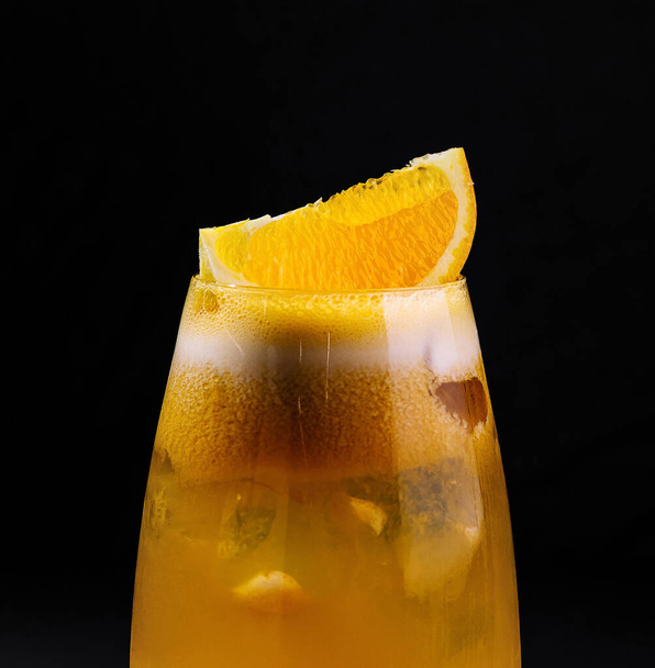 Κοντινό πλάνο ενός παγωμένου πορτοκαλιού κοκτέιλ γαρνιρισμένου με μια φέτα και σερβιρισμένου σε ένα κομψό ποτήρι - Φωτογραφία, εικόνα