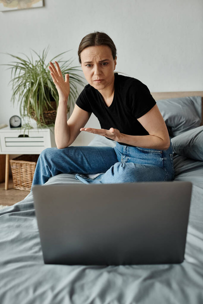 Woman sits on bed with laptop, seeking solace in virtual therapy. - Foto, Imagen
