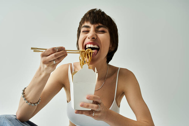 Stylish woman in a chic outfit gracefully eating noodles using chopsticks. - Fotografie, Obrázek