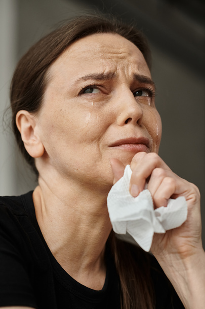 Middle-aged woman wipes her face with a tissue, dealing with mental distress. - Foto, immagini