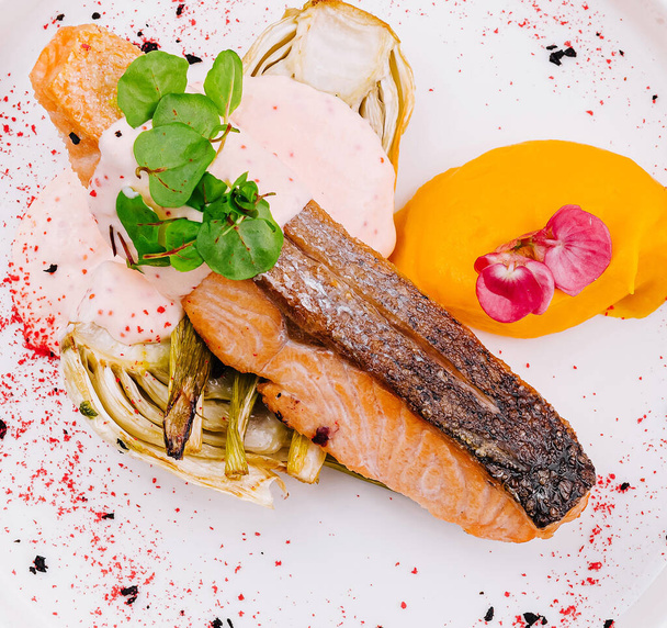 Vue de dessus d'un délicieux filet de saumon plaqué avec des légumes vibrants et de la sauce sur un fond blanc - Photo, image