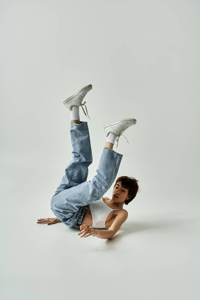 Young woman executing breakdance moves energetically on white background. - Foto, afbeelding
