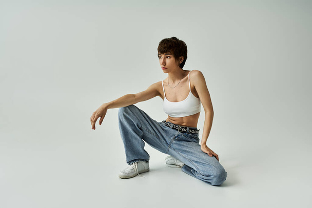 A stylish woman in white tank top and jeans poses gracefully on a white background. - Valokuva, kuva