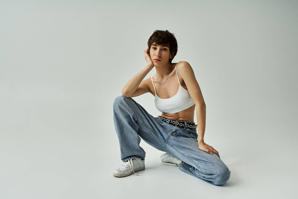 A stylish woman in a white tank top and jeans sitting gracefully on a white background. - Photo, image