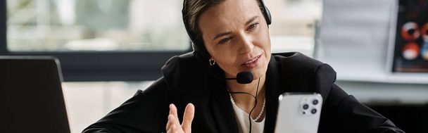 A middle-aged woman in distress listens with a headset at a desk. - Foto, imagen