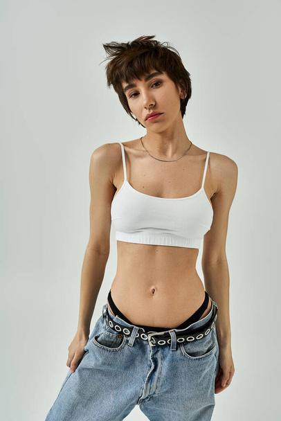 A stylish young woman posing gracefully in a white bra top and jeans. - Zdjęcie, obraz