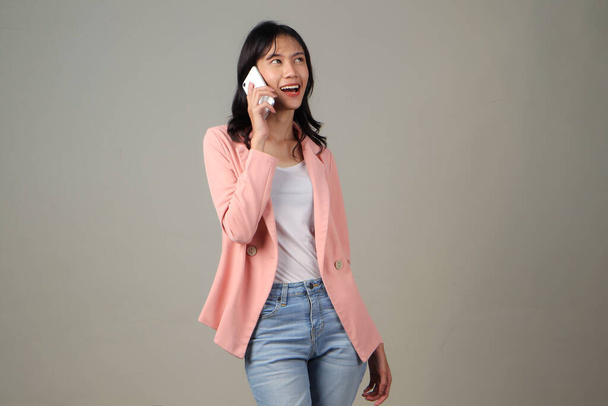 feliz asiático mujer hablando por teléfono con excitado expresión en su cara en aislado fondo - Foto, imagen