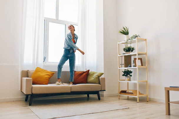 Mujer alegre saltando y bailando felizmente en su casa, relajándose en el sofá con música - Foto, imagen