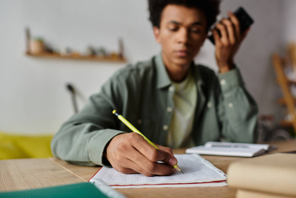 A young African American man sitting at a desk, writing in a notebook. - 写真・画像
