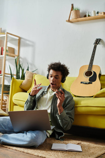Young man creating music online with guitar and laptop. - Fotó, kép