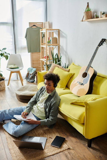 Young man, African American, sits near yellow couch with guitar. - Фото, изображение