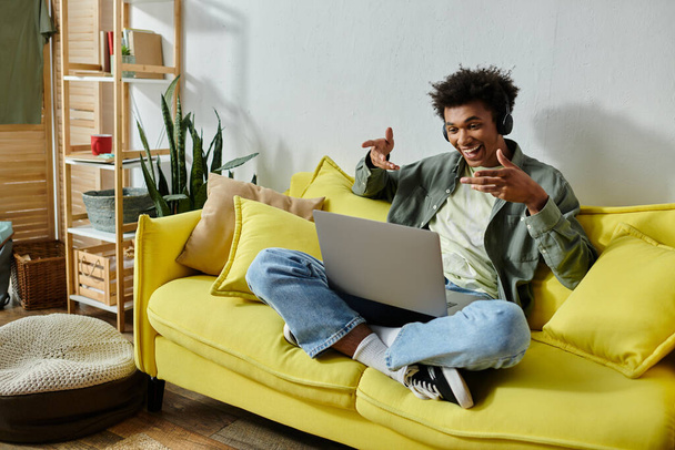 A young man engrossed in online studying, seated on a yellow couch with a laptop. - Foto, Imagem