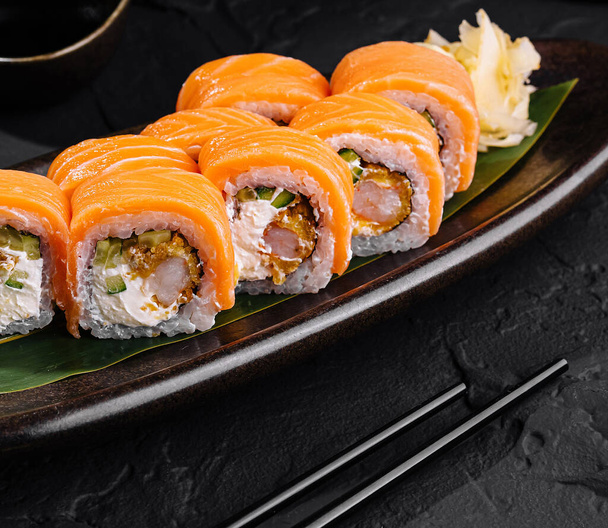 Delicioso sushi de salmón servido en un elegante plato oscuro con salsa de soja, perfecto para temas de cocina asiática - Foto, Imagen