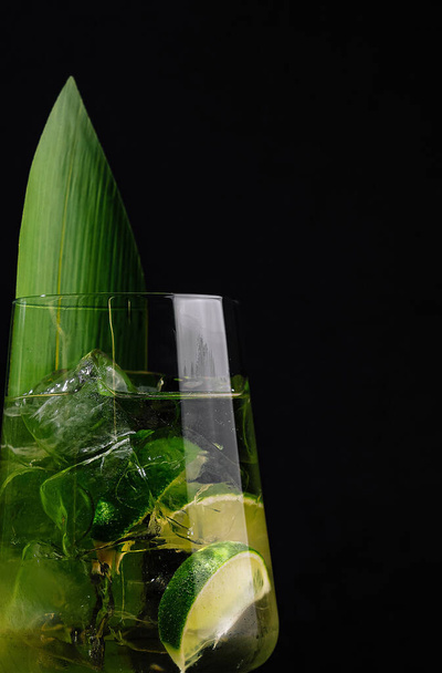 Elegantes Stielgutglas mit einem lebendigen Cocktail, garniert mit Limette und einem tropischen Blatt auf dunklem Hintergrund - Foto, Bild