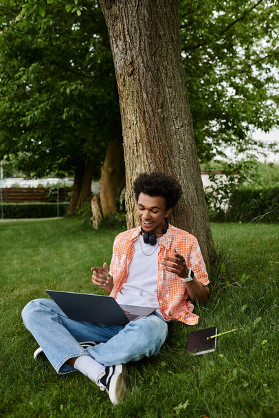 Young man, of African descent, using laptop while sitting under tree in park. - Fotografie, Obrázek