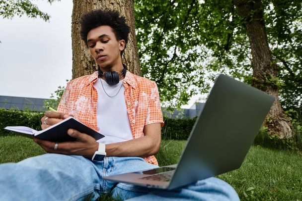 Young man immersed in work with laptop and headphones under tree. - Foto, Imagem