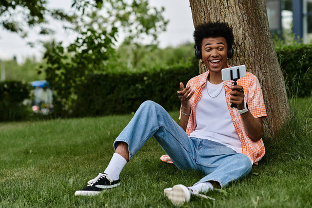 Young man sitting on grass, engrossed with cell phone. - Photo, Image