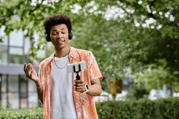 A young african american man enjoys the tranquility of a park while holding a cell phone. - Foto, imagen