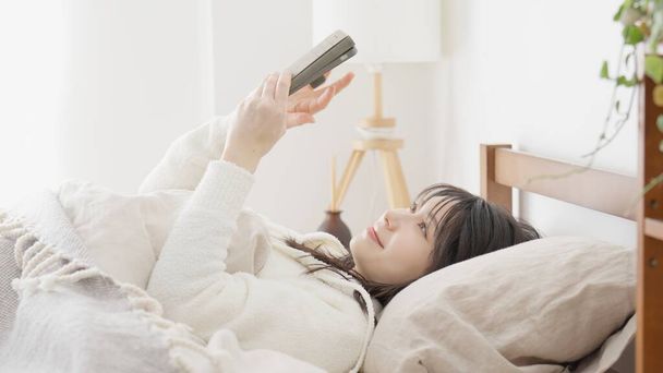 Femme asiatique regardant smartphone après le réveil - Photo, image