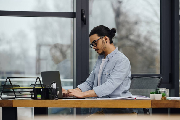 Un hombre profundamente centrado en su portátil mientras está sentado en un escritorio. - Foto, Imagen