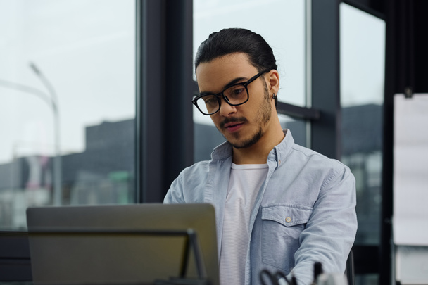 Un homme en lunettes se concentrant sur le travail sur un ordinateur portable dans un cadre de bureau. - Photo, image