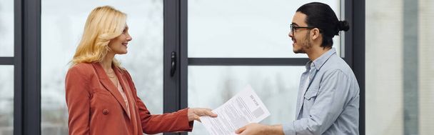 A man and woman exchanging documents in front of a window. - Photo, Image