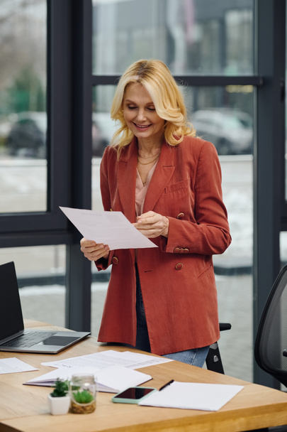 Μια γυναίκα στέκεται μπροστά σε ένα γραφείο γεμάτο χαρτιά, βαθιά στη σκέψη. - Φωτογραφία, εικόνα