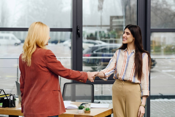 Две женщины пожимают друг другу руки в офисе, заключают сделку. - Фото, изображение