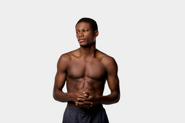 Ένας ημίγυμνος Αφροαμερικάνος στέκεται με αυτοπεποίθηση πάνω σε ένα λευκό φόντο σε ένα στούντιο.. - Φωτογραφία, εικόνα