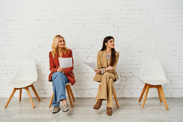 Μια ομάδα γυναικών κάθεται με χάρη σε καρέκλες μπροστά από έναν τοίχο από τούβλα. - Φωτογραφία, εικόνα
