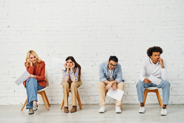 Un grupo diverso de personas sentadas frente a una pared blanca en blanco, posando y conversando. - Foto, imagen