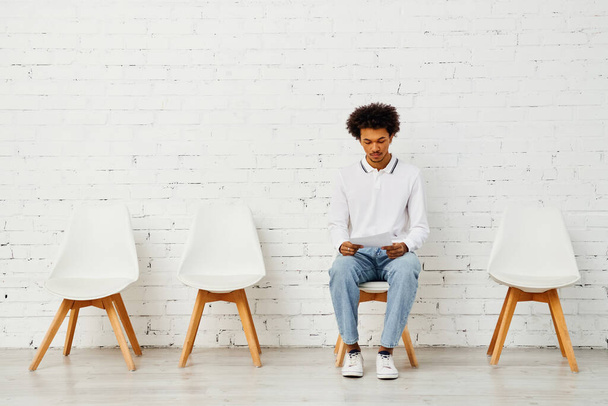 Άνδρας που περιβάλλεται από λευκές καρέκλες σε μια καλλιτεχνική επίδειξη μοναξιάς. - Φωτογραφία, εικόνα