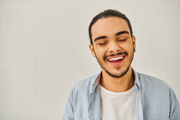Een jonge man lacht terwijl hij naar een blanco witte achtergrond kijkt. - Foto, afbeelding