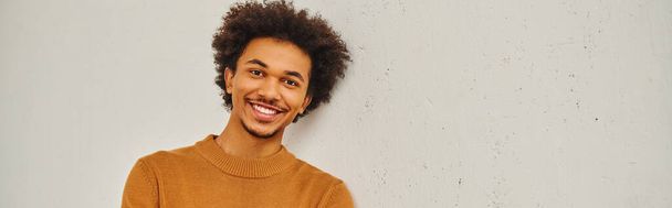 Young man with curly hair smiles in front of a white wall. - Photo, Image
